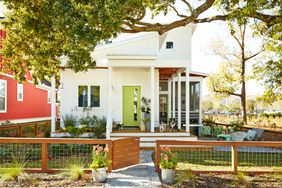 a small modern white house with a green door and a wire fence