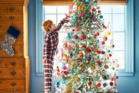 Little boy puts an ornament on a Christmas tree