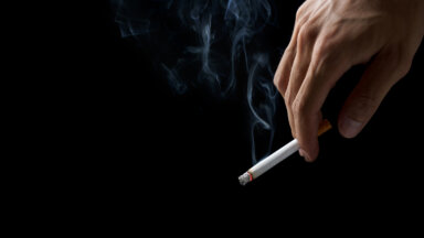 Closeup hand of man holding a cigarette.Tobacco cigarette Butt on the Floor in dark background for world Tobacco day concept or stop smoking