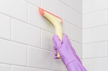 person using a squeegee in shower to prevent mold and mildew
