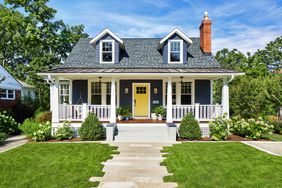 a small cute house with a yellow door and large front porch