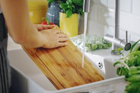 person washing wooden cutting board in sink
